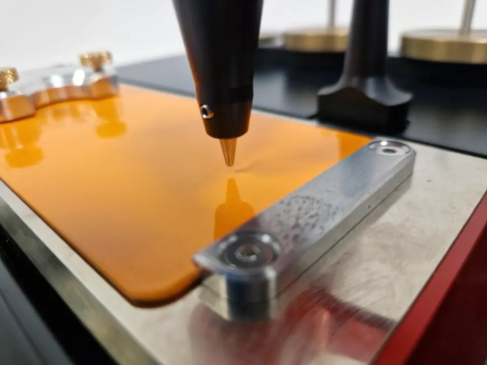 Close-up of a 3D printer nozzle extruding orange filament onto the print bed.